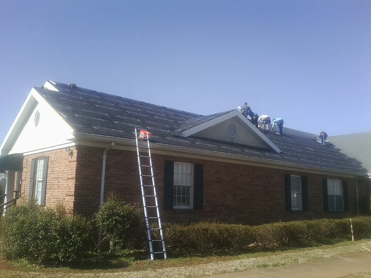 Crew tearing shingles off a brick ranch roof with a ladder set — Metal Roof Repair work by our crew in Bell Buckle