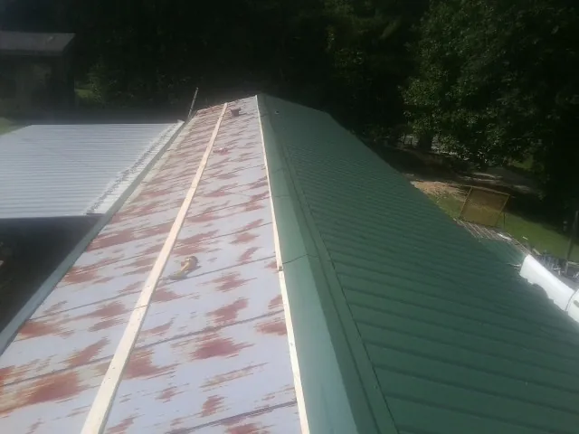 Old rusted panels beside newly installed green metal roofing — Wind Damage Roof Repair by Roofing Brothers in Bell Buckle
