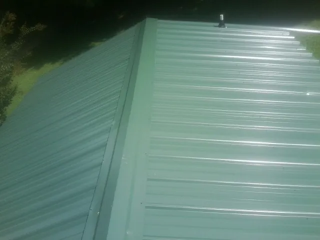 New green metal panels meeting at the ridge of a roof — Flat Roof Repair work by our crew in Bell Buckle