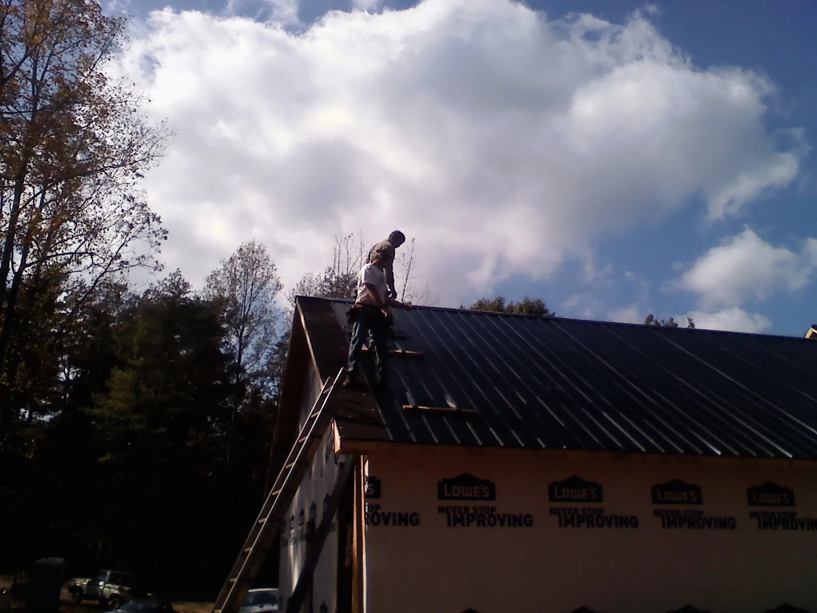 Roofer fastening dark metal panels high against a cloudy sky, from a Roof Inspection job in Bell Buckle