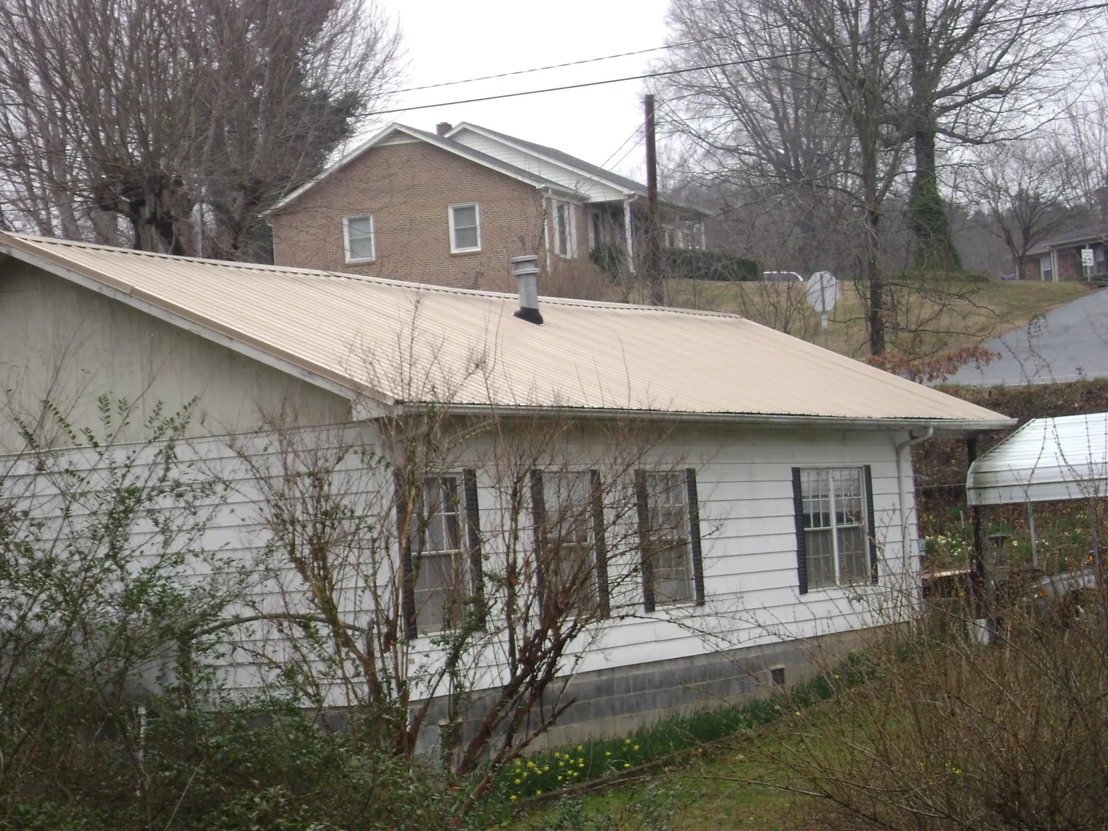 Tan metal roof on a white sided house set into a hillside — Commercial Roofing by Roofing Brothers in Bell Buckle