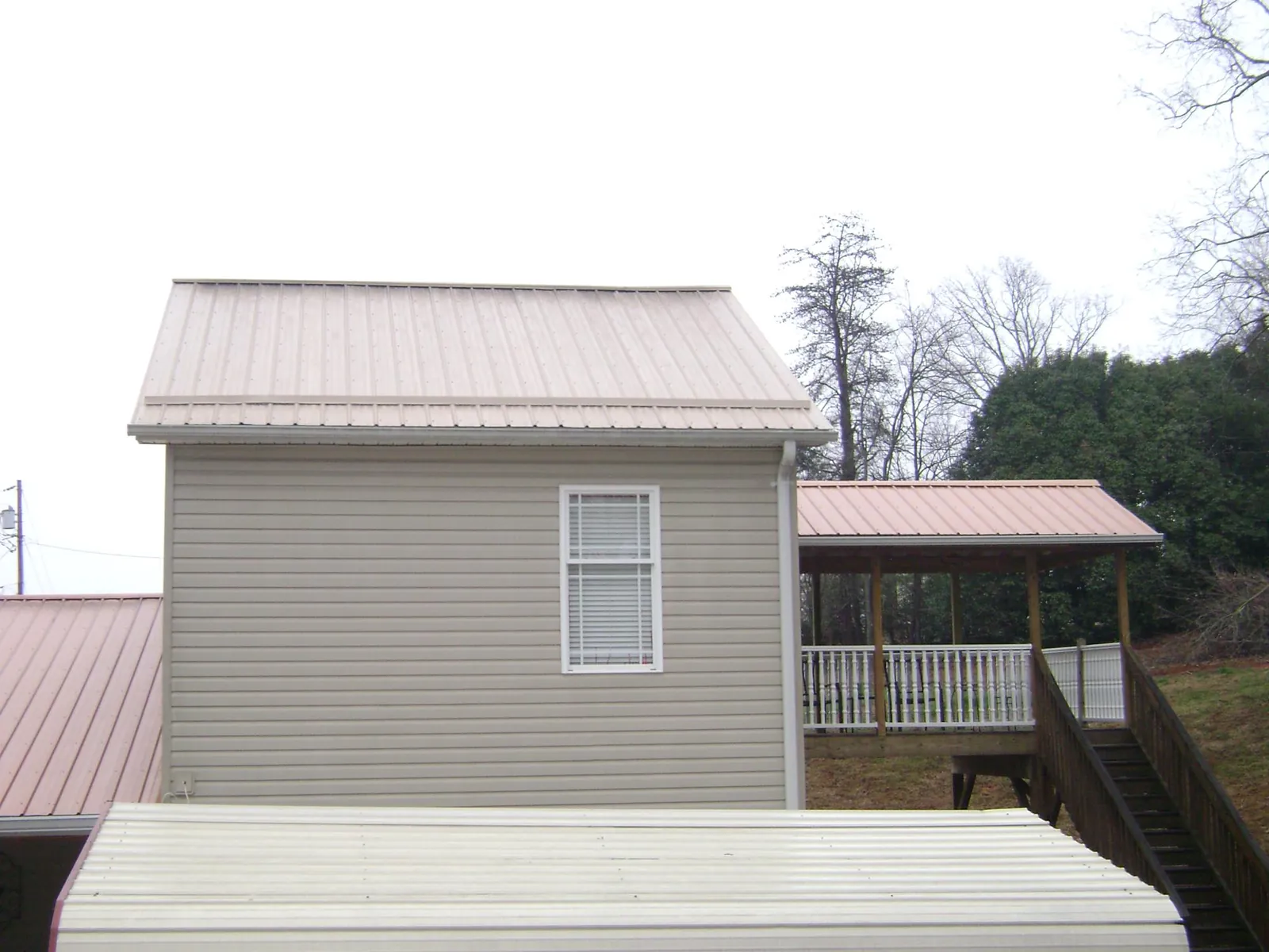 Tan metal roofs on a two story addition and attached porch, from a Roof Replacement job in Bell Buckle